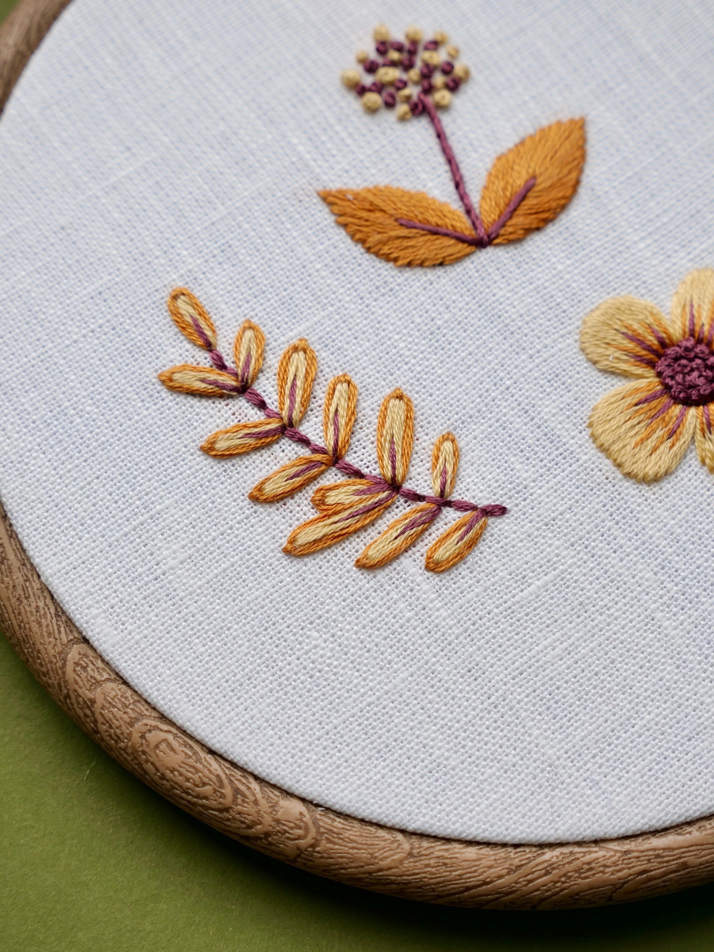 Detalj av håndbrodert blomstermotiv på hvit stoff i tre-ramme