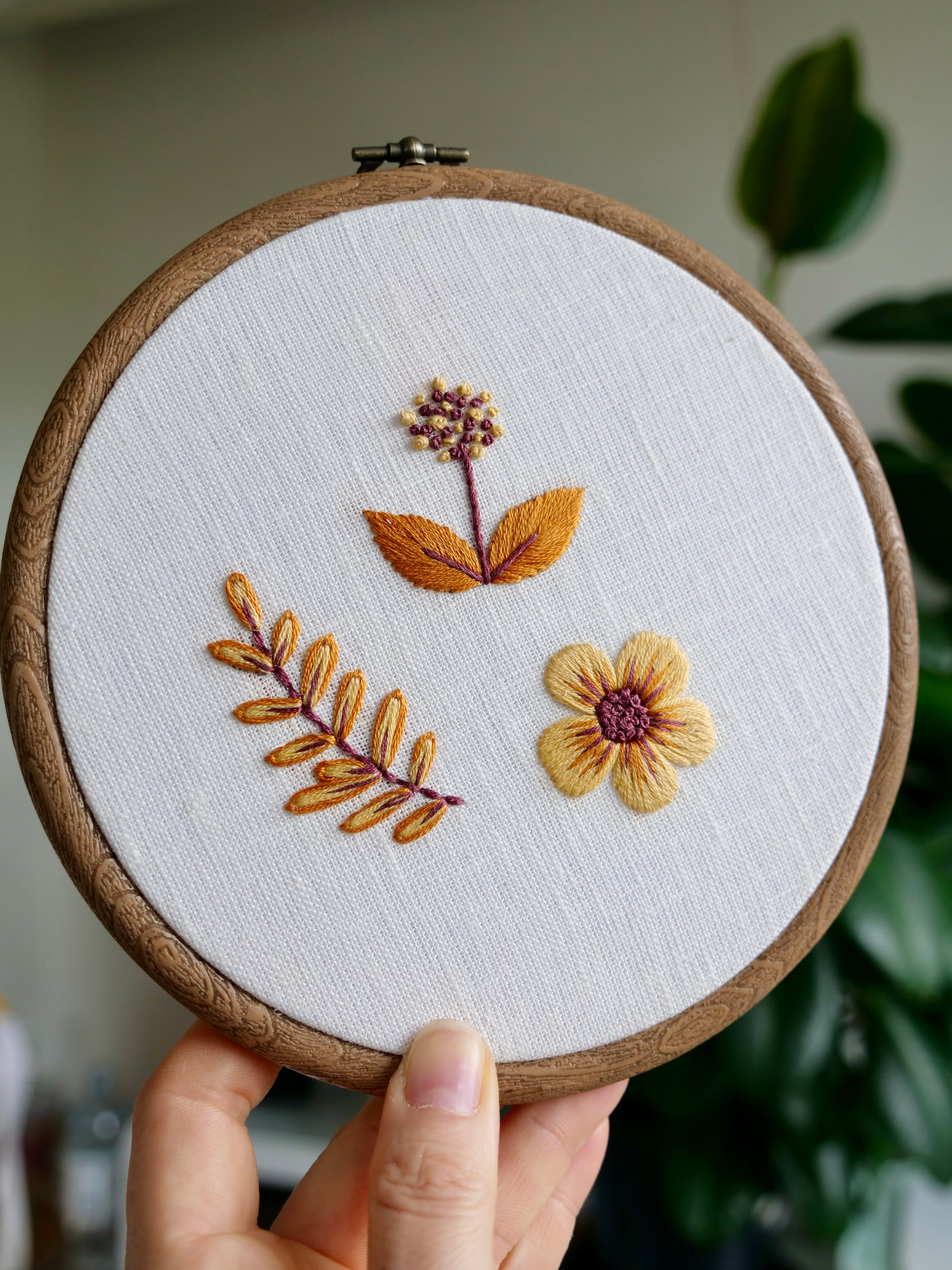 Hånd som holder en broderiramme med gul og burgunder blomsterbroderi